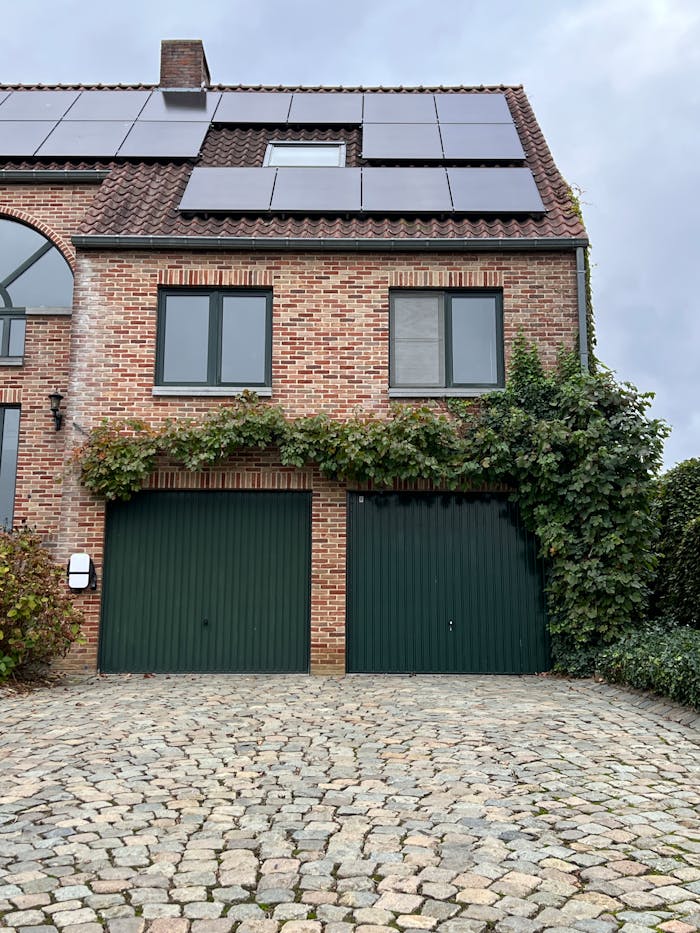 Charming brick house with solar panels and ivy-covered garage. Eco-friendly architecture.