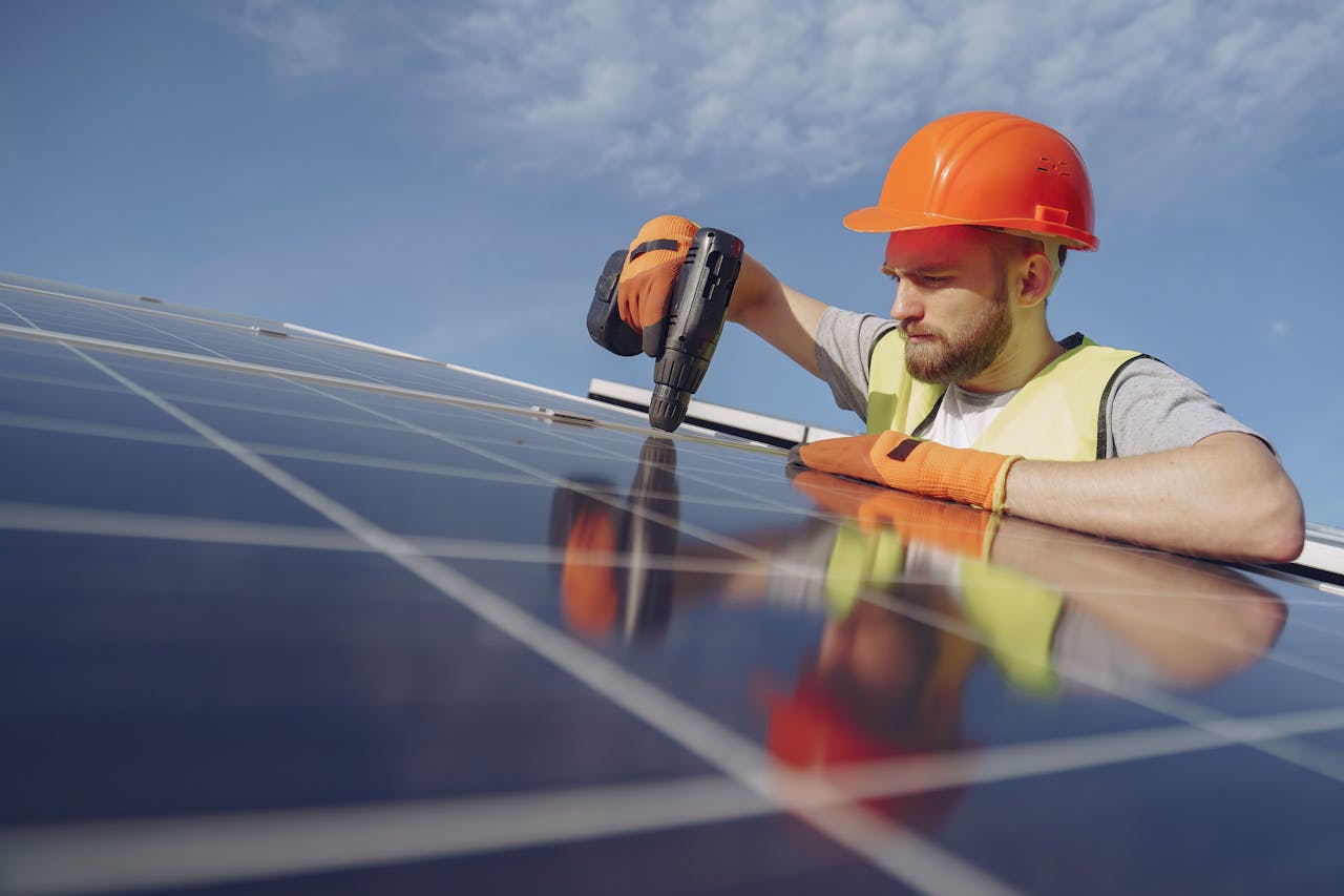 gallery-05 Low angle of serious bearded male electrician in hardhat and protective gloves installing solar photovoltaic panel system using drill